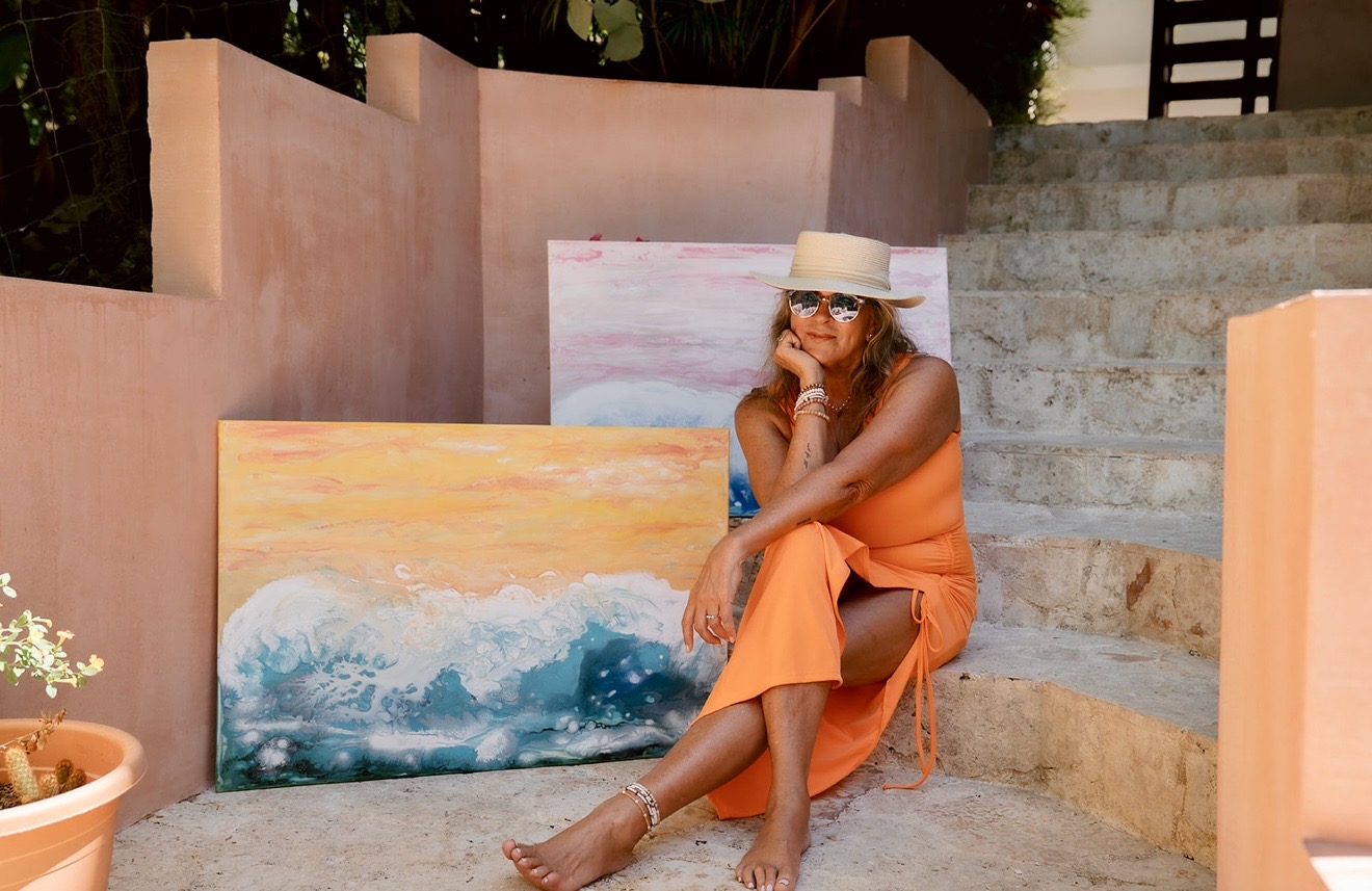 Lori Burke sitting on stone steps with two of her wave paintings