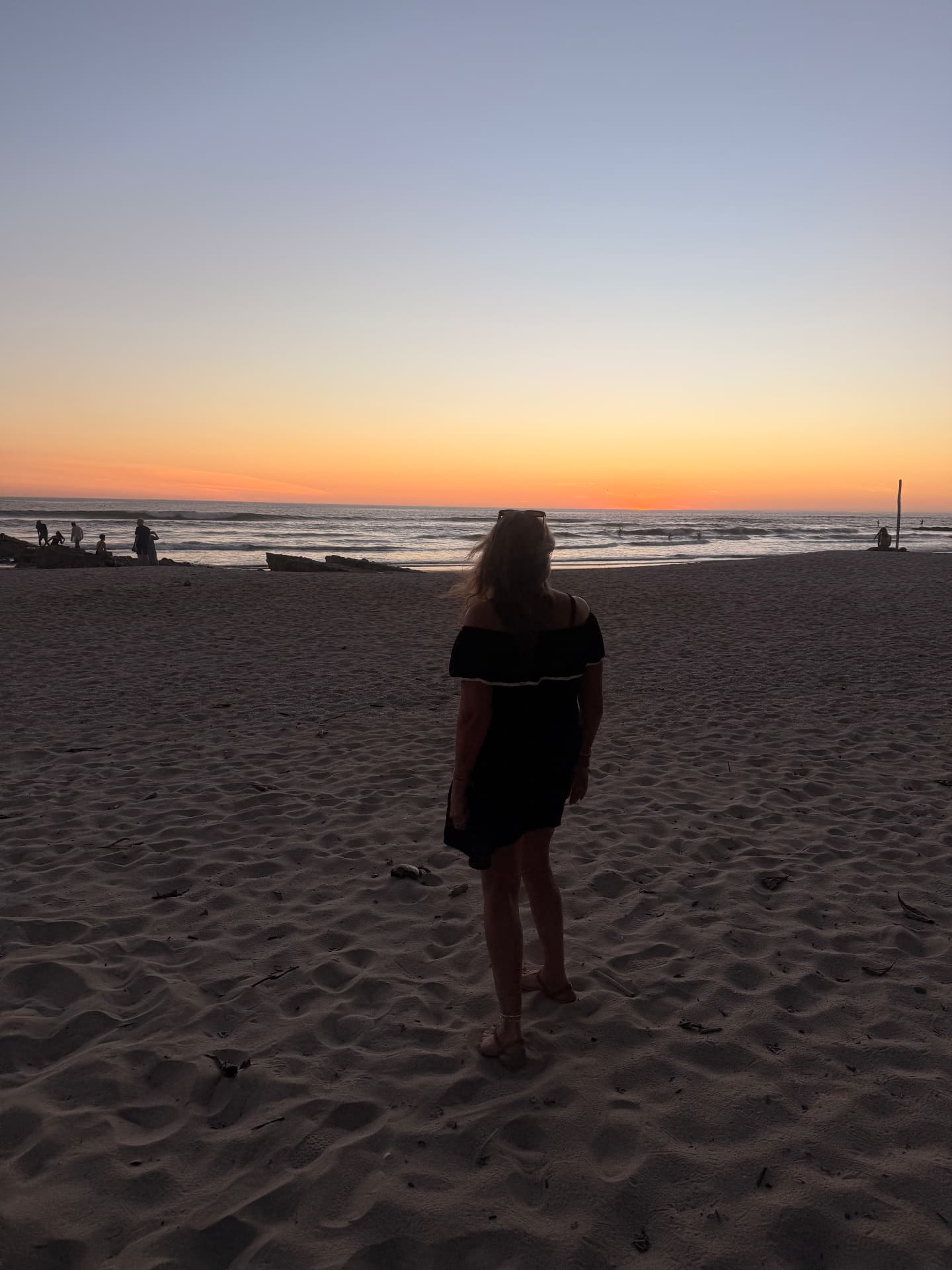Lori seen from behind, standing on the sand at dusk, watching the sunset over the ocean